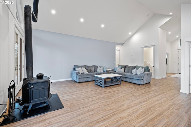 living room featuring a wood stove, light hardwood / wood-style flooring, and high vaulted ceiling