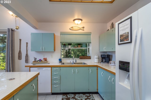 kitchen featuring white appliances, sink, light tile floors, and tile counters