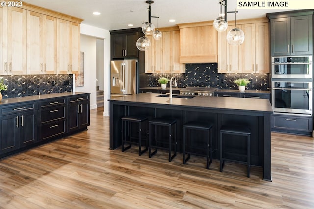 kitchen with pendant lighting, a kitchen island with sink, appliances with stainless steel finishes, and light brown cabinetry