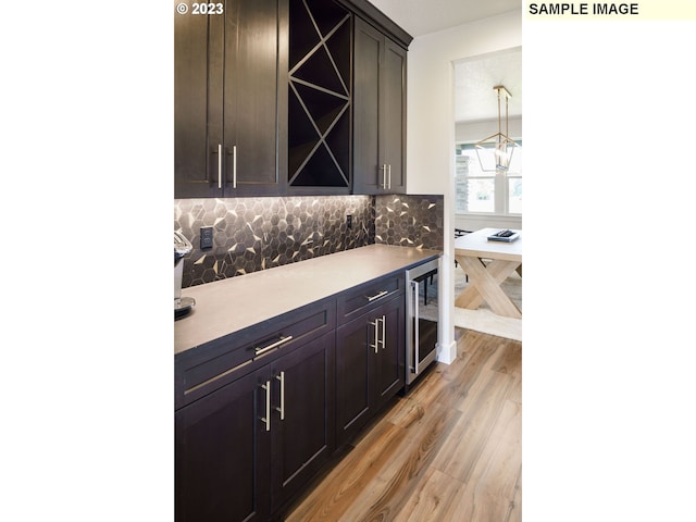 bar featuring light hardwood / wood-style floors, hanging light fixtures, decorative backsplash, dark brown cabinetry, and beverage cooler