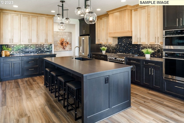 kitchen featuring premium appliances, sink, decorative light fixtures, a center island with sink, and light brown cabinets