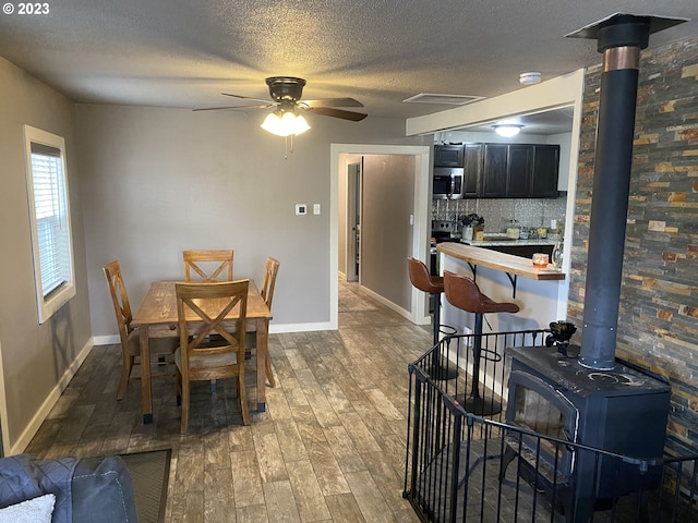 dining area with dark hardwood / wood-style flooring, ceiling fan, a wood stove, and a textured ceiling