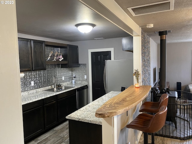 kitchen with light stone countertops, appliances with stainless steel finishes, a kitchen bar, sink, and light hardwood / wood-style flooring