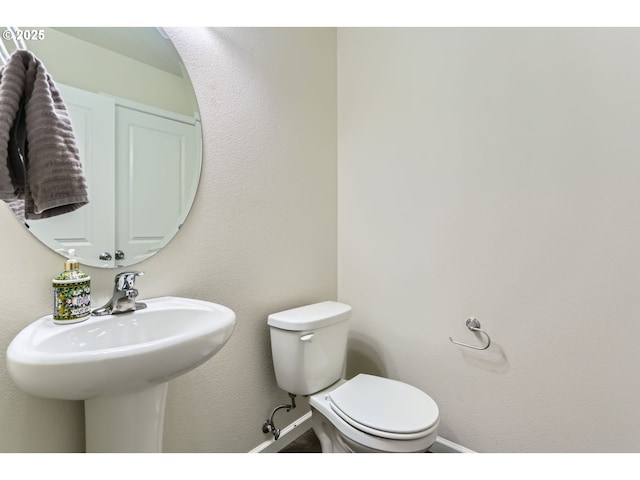 half bath with toilet, baseboards, and a sink