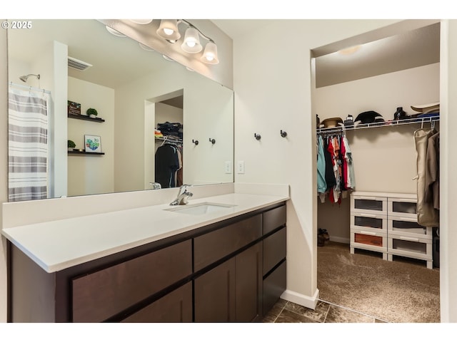 bathroom featuring vanity, baseboards, a walk in closet, and visible vents