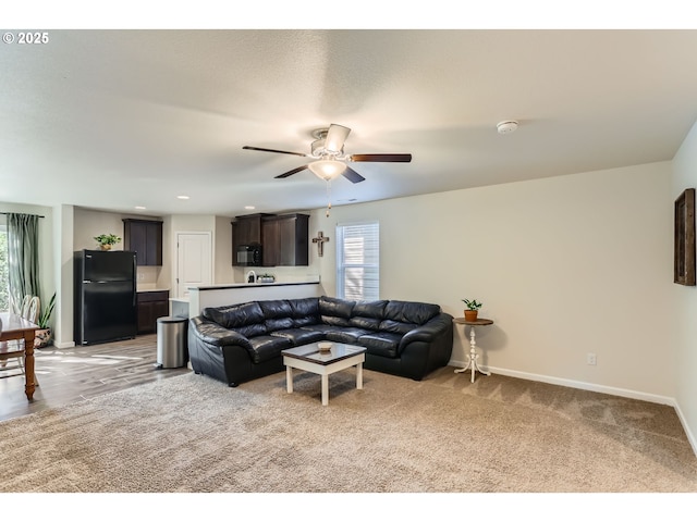 living area with baseboards, a ceiling fan, and light colored carpet