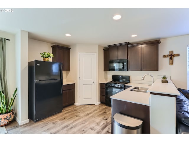 kitchen with dark brown cabinets, a sink, light countertops, black appliances, and light wood-style floors