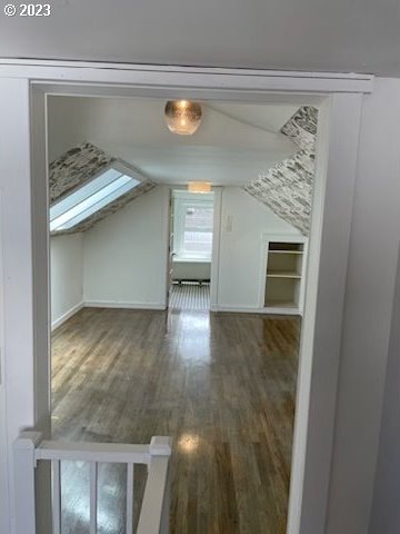 bonus room featuring built in shelves, vaulted ceiling with skylight, and dark wood-type flooring