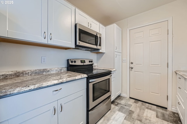 9832 N Clarendon Ave, Portland, OR 97203 - kitchen with appliances with stainless steel finishes, light wood-type flooring, white cabinetry, and light stone counters