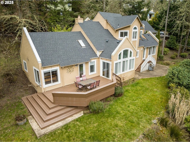 rear view of house with a wooden deck, a lawn, a chimney, and roof with shingles