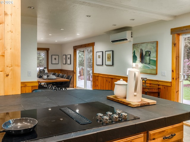 kitchen featuring beam ceiling, wooden walls, black electric stovetop, and a wall unit AC