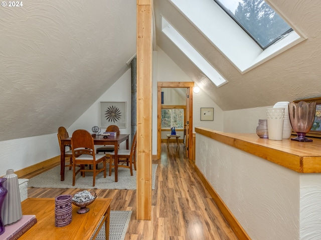 additional living space with wood-type flooring, vaulted ceiling with skylight, and a textured ceiling