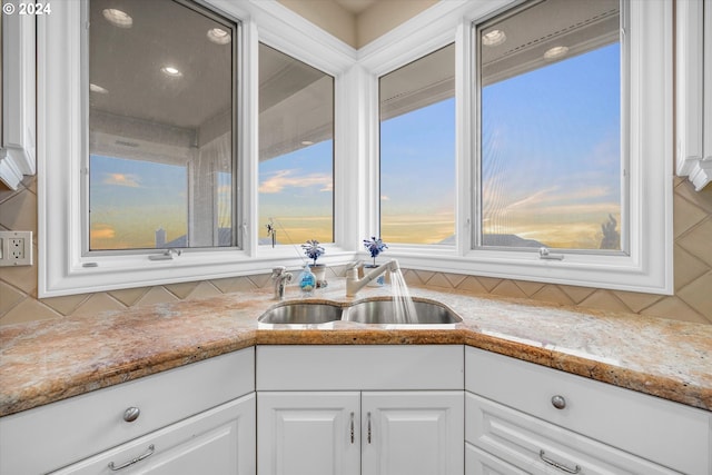 kitchen featuring sink, light stone counters, tasteful backsplash, and white cabinetry