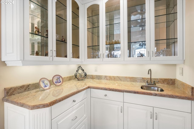 bar with sink, light stone counters, and white cabinetry