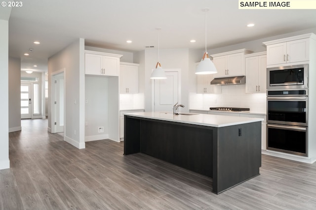 kitchen with appliances with stainless steel finishes, white cabinetry, tasteful backsplash, and an island with sink