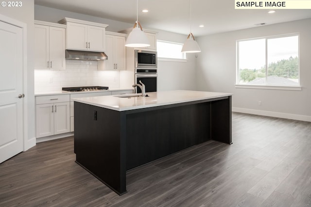 kitchen featuring decorative light fixtures, appliances with stainless steel finishes, a center island with sink, white cabinetry, and dark hardwood / wood-style floors