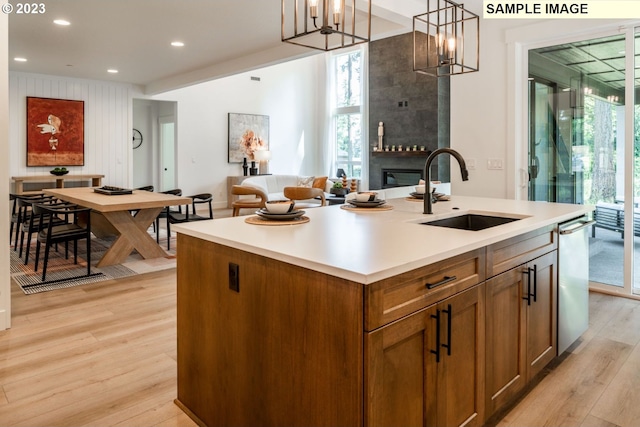 kitchen with a fireplace, a notable chandelier, sink, an island with sink, and light wood-type flooring