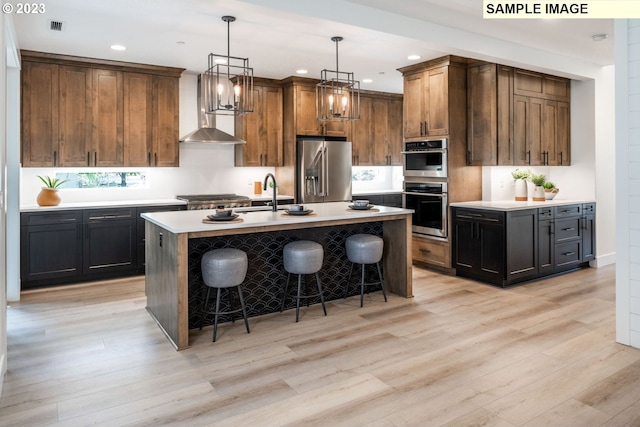 kitchen featuring a kitchen island with sink, a kitchen bar, light hardwood / wood-style flooring, stainless steel appliances, and pendant lighting