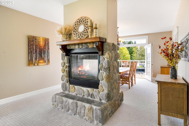 carpeted living room with a stone fireplace and a notable chandelier