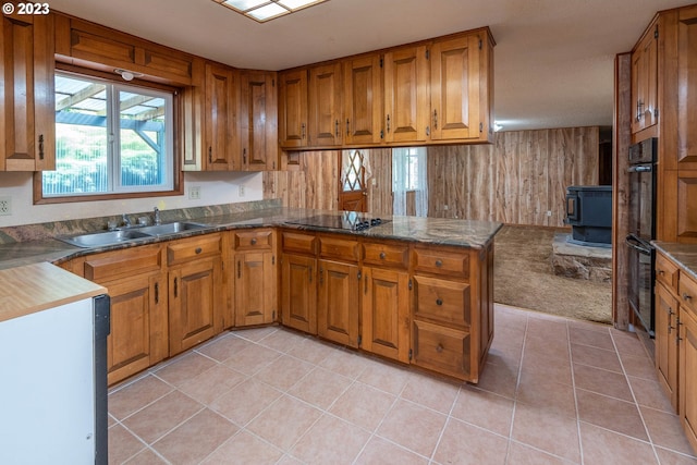 kitchen featuring kitchen peninsula, black appliances, a wood stove, light tile flooring, and sink