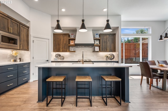 kitchen with a kitchen breakfast bar, light countertops, open shelves, stainless steel microwave, and custom range hood