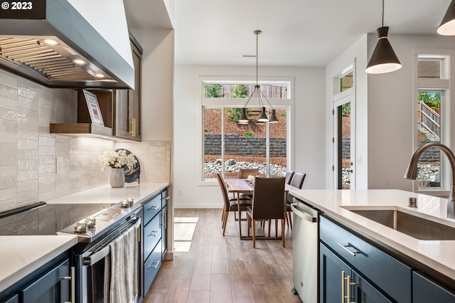 kitchen featuring pendant lighting, stainless steel appliances, a sink, blue cabinets, and wall chimney exhaust hood