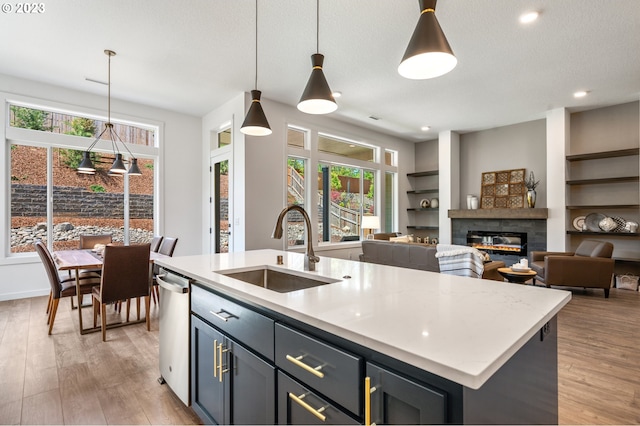 kitchen featuring a glass covered fireplace, a kitchen island with sink, light countertops, light wood-style floors, and a sink