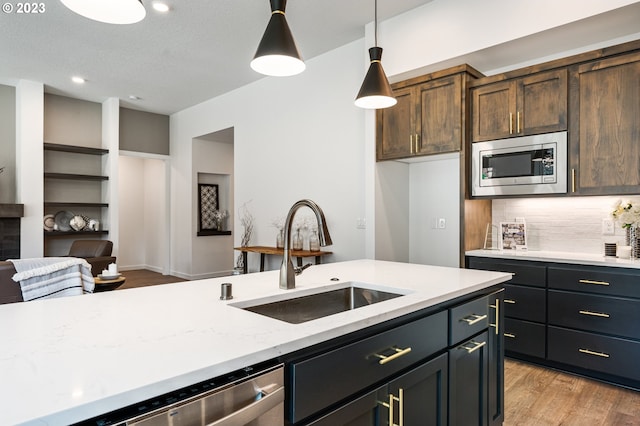 kitchen with a sink, appliances with stainless steel finishes, light wood-type flooring, backsplash, and pendant lighting