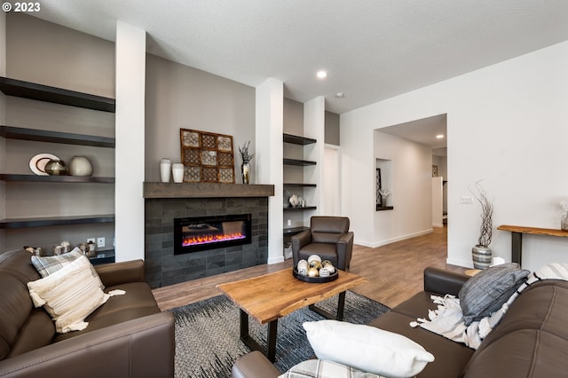 living room with a textured ceiling, built in shelves, a fireplace, wood finished floors, and baseboards