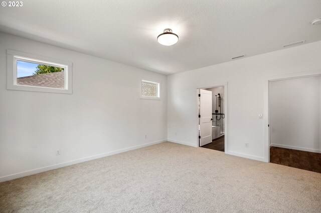 empty room featuring visible vents, dark carpet, a textured ceiling, and baseboards