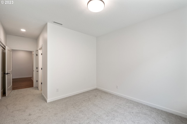 spare room featuring light colored carpet, visible vents, and baseboards