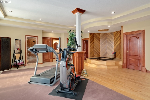 exercise area featuring a tray ceiling, light hardwood / wood-style floors, and ornate columns