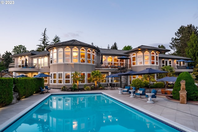 back house at dusk with a balcony and a patio area