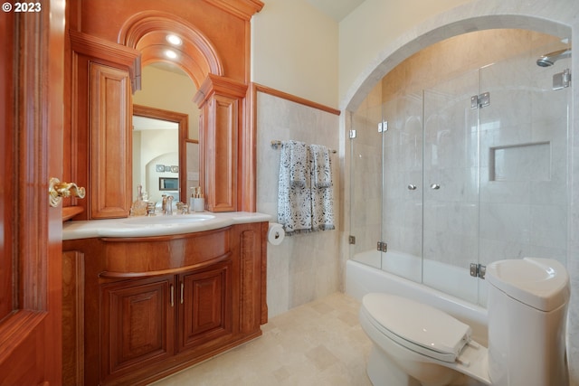 full bathroom with bath / shower combo with glass door, tile flooring, toilet, vanity, and tile walls