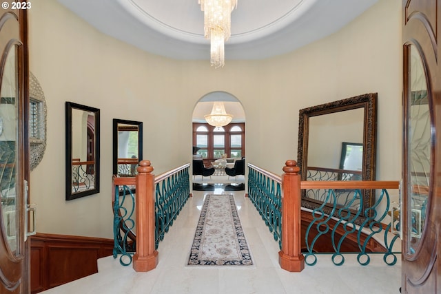 corridor with light tile flooring, a raised ceiling, a chandelier, and a towering ceiling