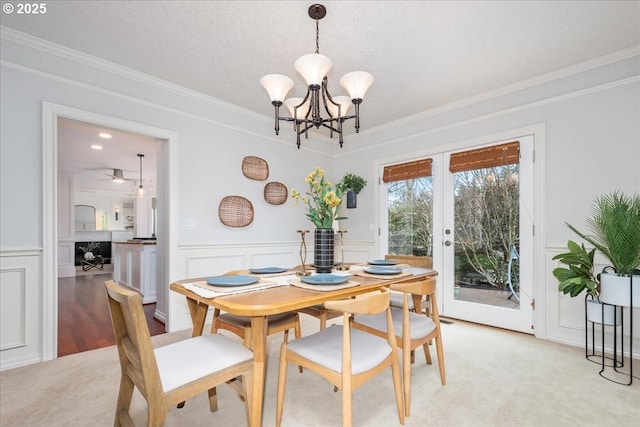 dining space with ornamental molding, a chandelier, french doors, a wainscoted wall, and a decorative wall