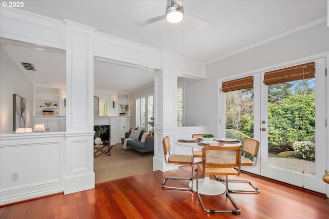interior space with crown molding, ceiling fan, a fireplace, visible vents, and wood finished floors