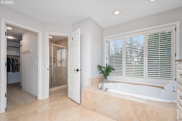 bathroom featuring a walk in closet, a garden tub, and a shower stall