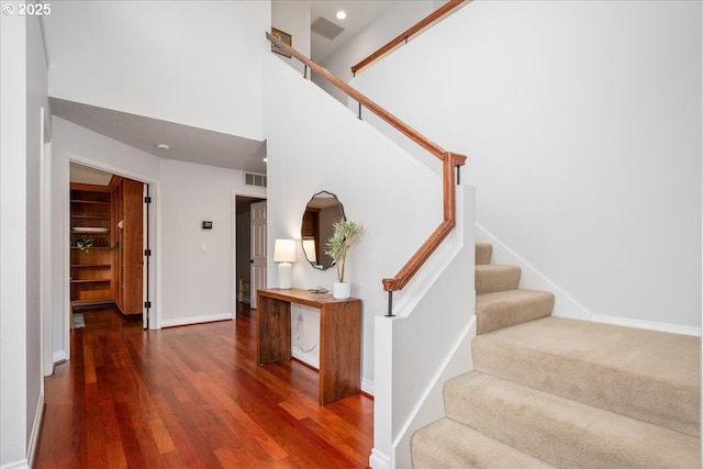 staircase with visible vents, baseboards, wood finished floors, and a towering ceiling