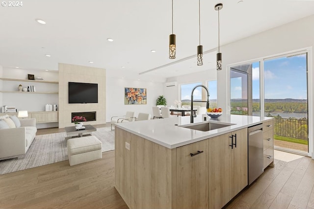 kitchen with pendant lighting, light hardwood / wood-style floors, sink, stainless steel dishwasher, and a center island with sink