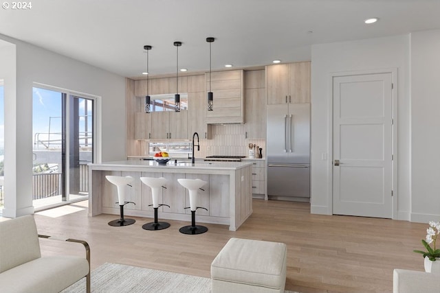 kitchen featuring built in fridge, a center island with sink, pendant lighting, and light brown cabinetry