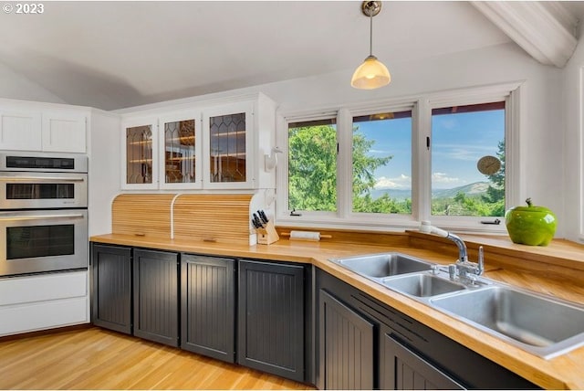 kitchen with stainless steel double oven, light hardwood / wood-style floors, sink, white cabinets, and pendant lighting