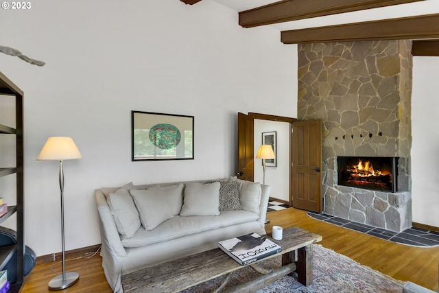 living room with beamed ceiling, hardwood / wood-style flooring, and a stone fireplace