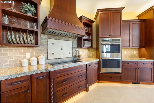 kitchen with light stone counters, backsplash, double oven, premium range hood, and black electric stovetop