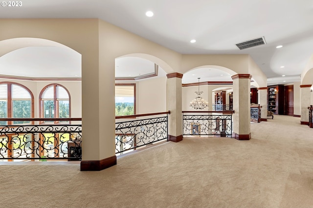 hall featuring carpet floors, a raised ceiling, decorative columns, and crown molding