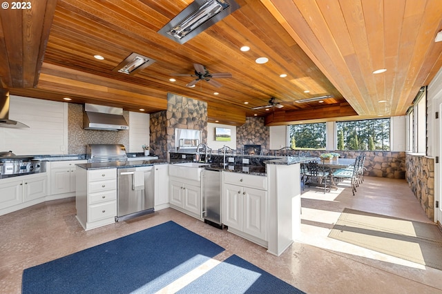 kitchen featuring wooden ceiling, ceiling fan, kitchen peninsula, wall chimney exhaust hood, and white cabinets