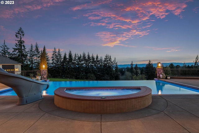 pool at dusk with a patio, an in ground hot tub, and a water slide