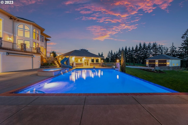 pool at dusk with a water slide, an outdoor hot tub, and a yard