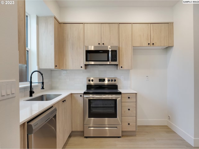 kitchen with appliances with stainless steel finishes, light brown cabinets, light hardwood / wood-style floors, and sink