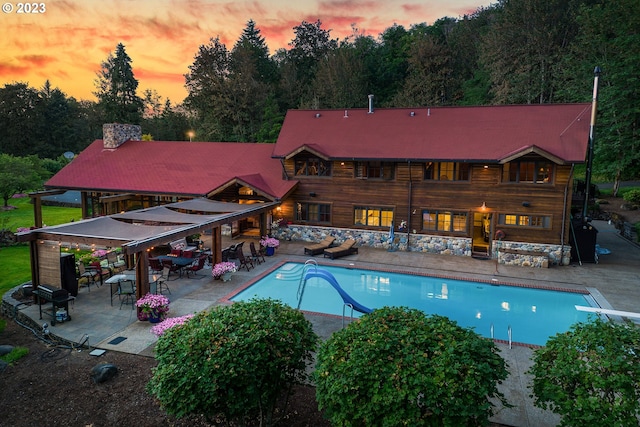 pool at dusk featuring a diving board, a water slide, and a patio area